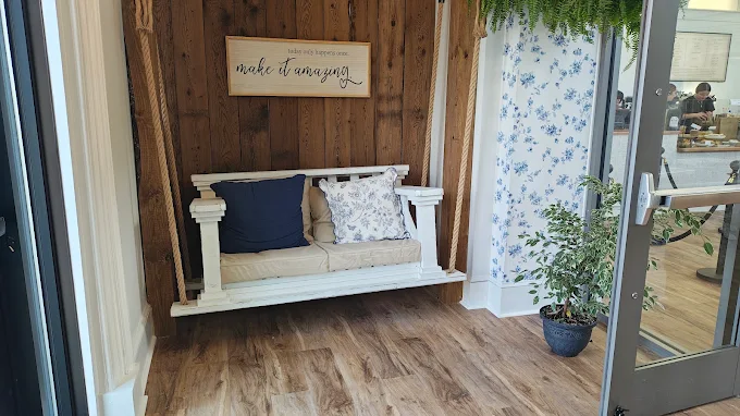 A white porch swing hung on rope against a reclaimed wood wall, with a navy pillow and a sign that reads make it amazing